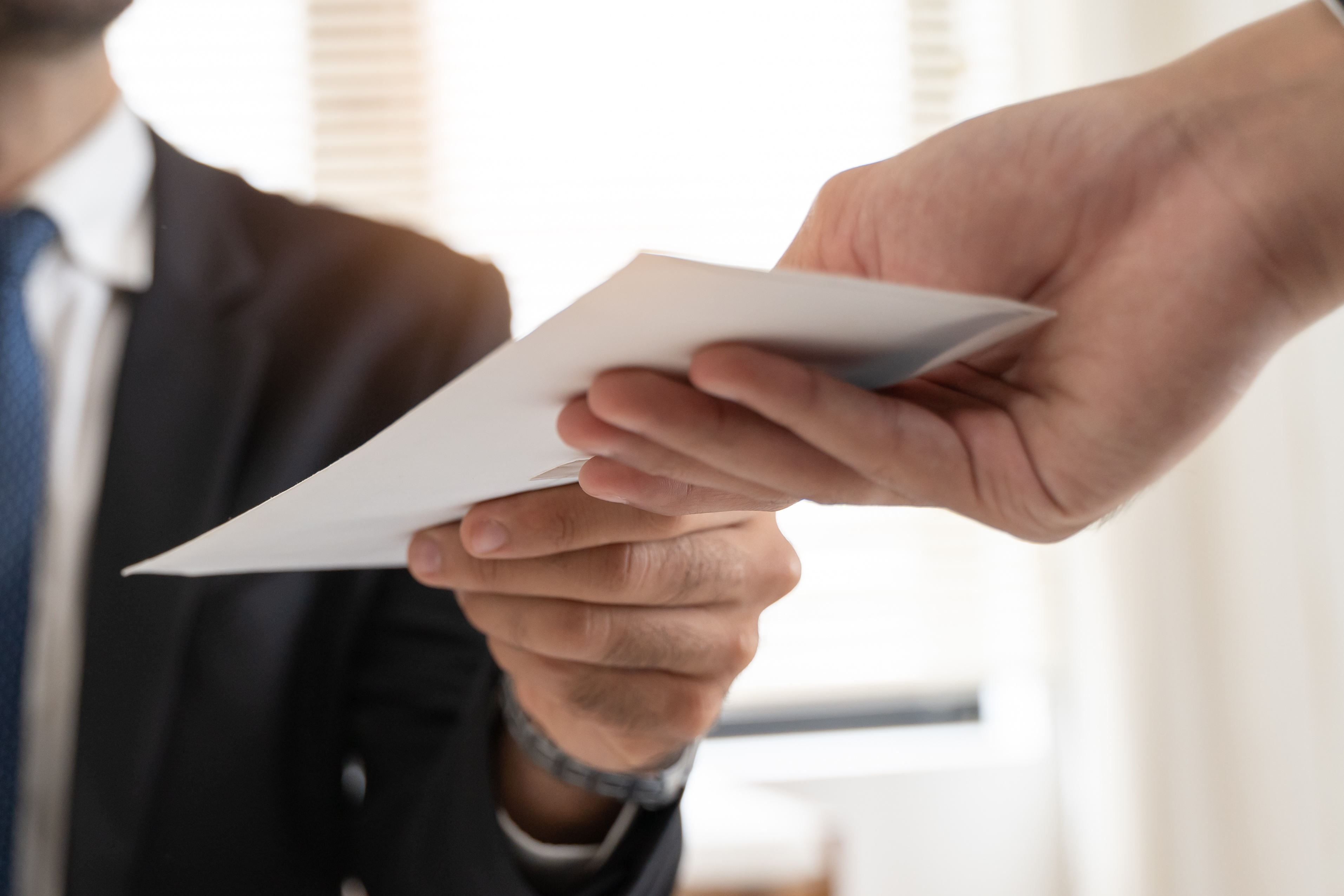 Two businesspeople exchanging a white envelope in a professional setting